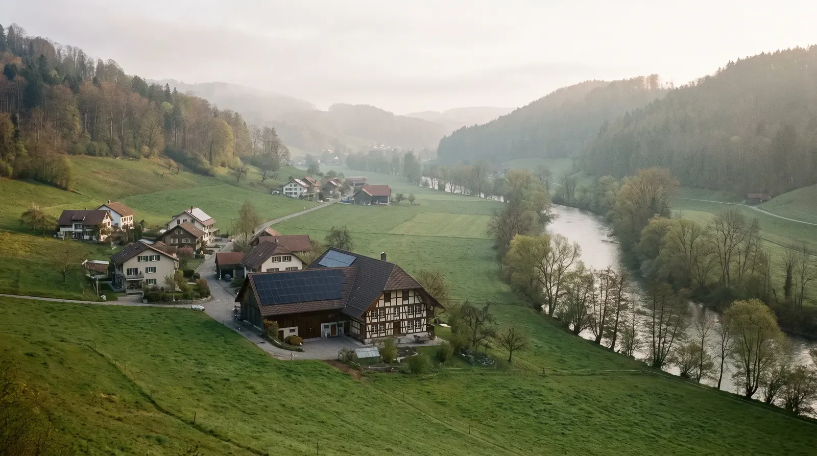Weiler im Aaretal mit einem Bauernhaus, dessen Ziegeldach eine Solaranlage trägt, daneben Wiesen und die Aare mit Uferbäumen