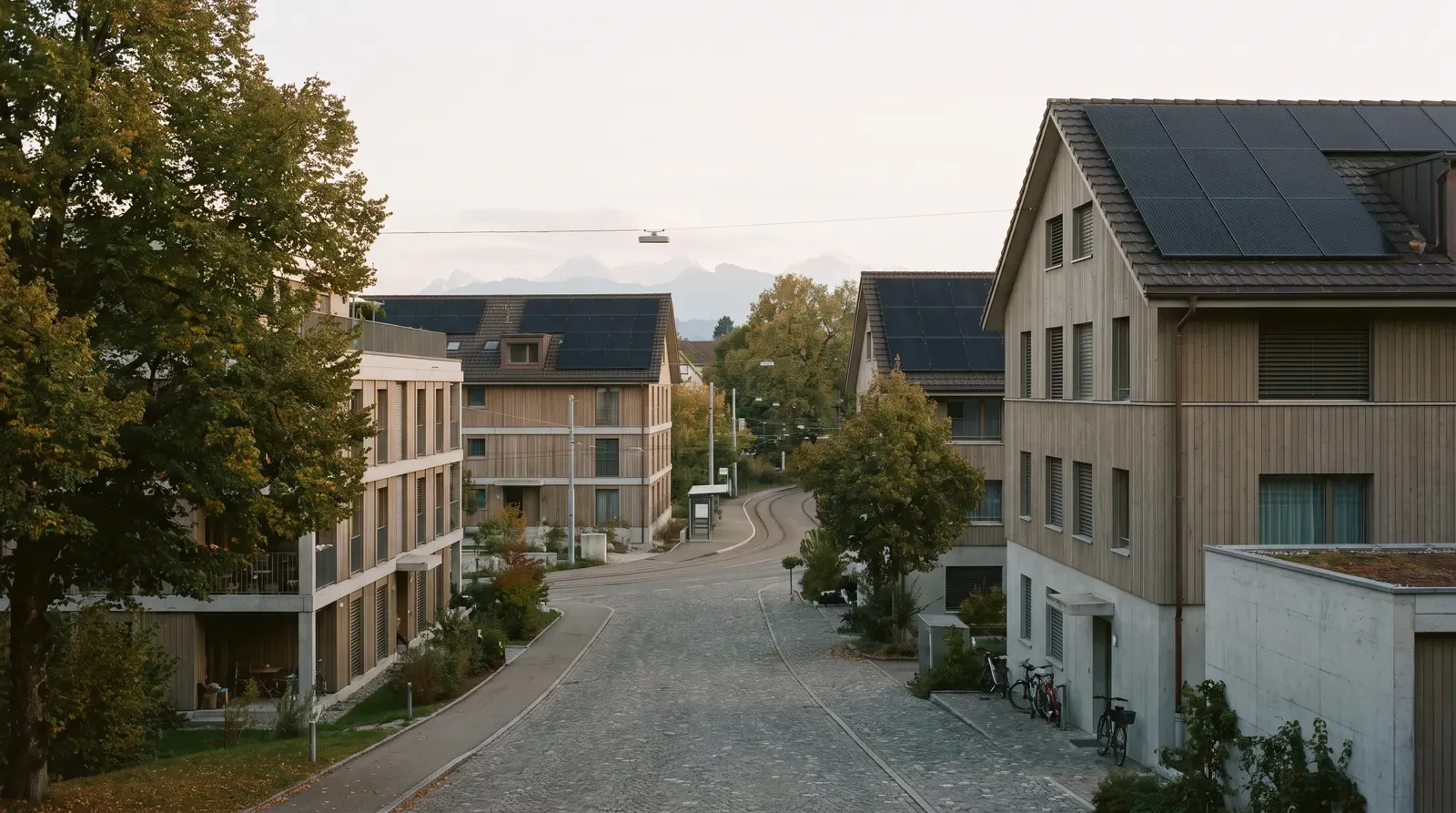 Strasse in einem Berner Vorort mit Mehrfamilienhäusern aus Holz, auf den Ziegeldächern schwarze Solarmodule, im Hintergrund die Alpen