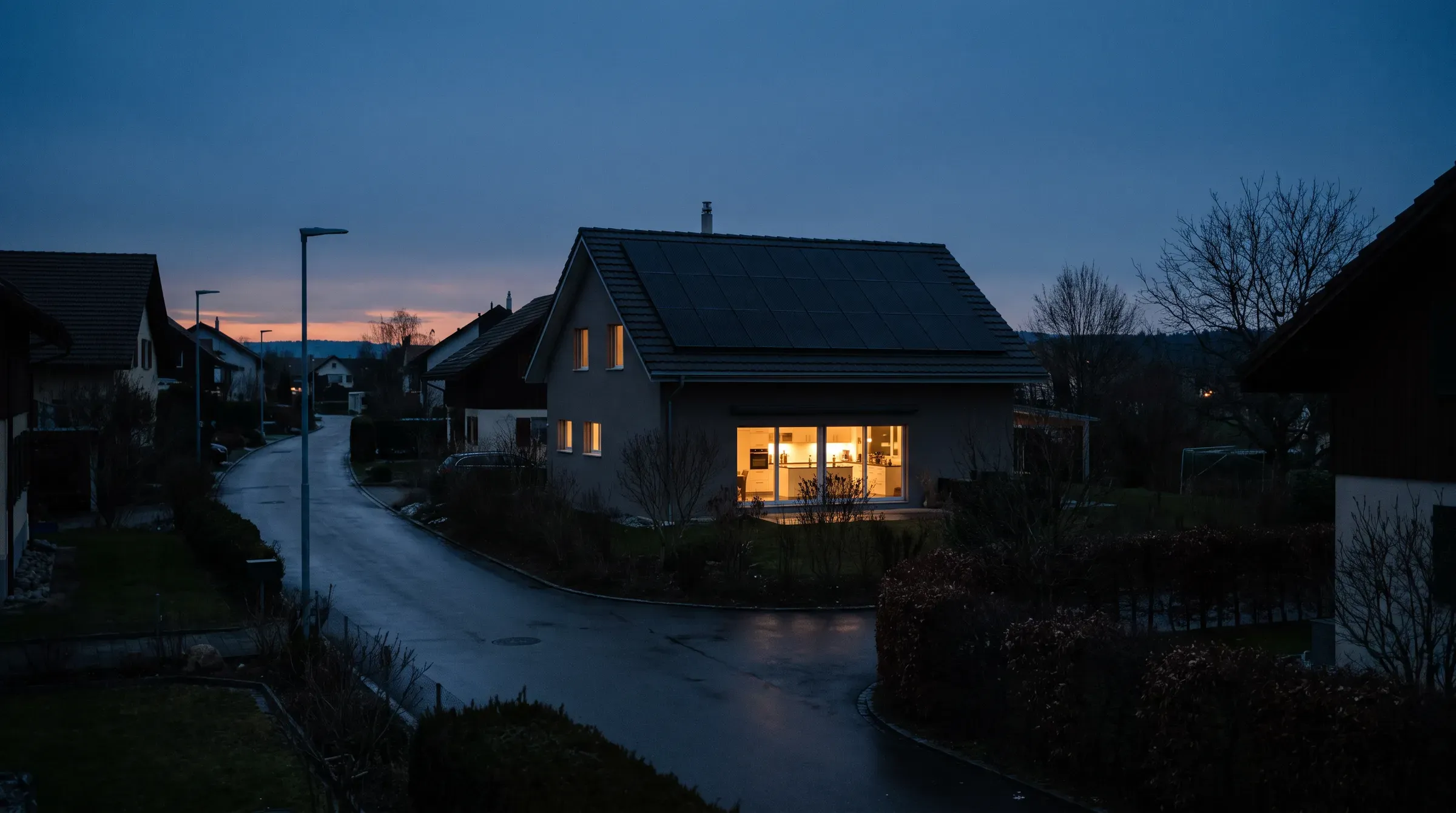 Quartierstrasse bei einem Stromausfall in der Dämmerung, ein Haus mit Solaranlage hat noch Licht in der Küche
