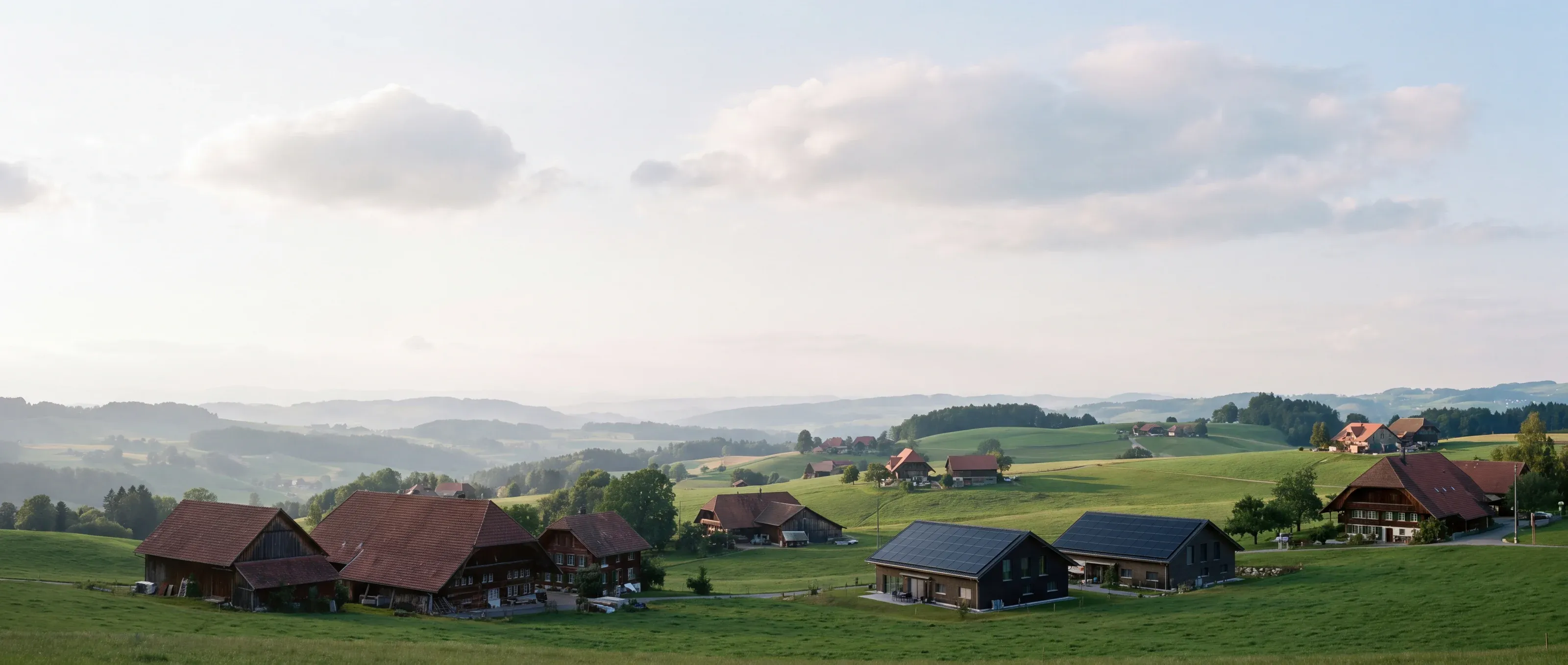 Hügellandschaft mit Bauernhäusern, zwei Häuser tragen schwarze Solaranlagen auf dem Dach